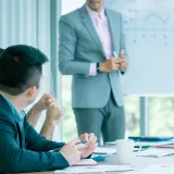 ホワイトボードの前で話す男性と、それを聞く男性
